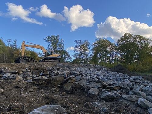 Excavator moving stones on work site in Lee, MA Excavator moving stones on work site in Lee, MA